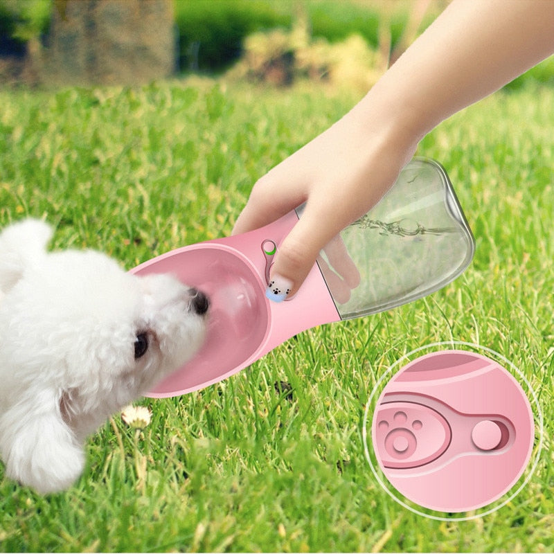 Small white dog (Bichon Frise) drinking from pink Portable Pet Water Bottle on grass, with close-up inset of one-touch button